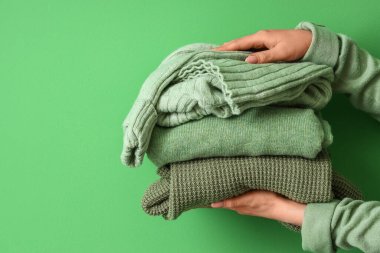 Renkli arka planda bir yığın süveter tutan kadın