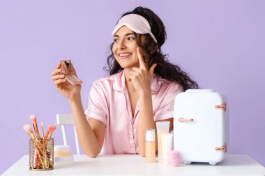 Buzdolabı ve kozmetik ürünleriyle dolu masaların yanında yüzü kızaran bir kadın var.