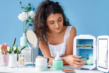 Açık buzdolabı ve renkli duvarın yanında kozmetik ürünleri olan güzel bir kadın.