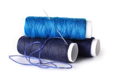 Mavi dikiş ipliği makaraları ve beyaz arkaplanda iğne