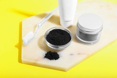 Sarı arka planda aktif kömür diş tozu ve diş fırçası olan kase.