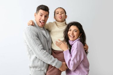 Küçük kız ve ailesi sıcak süveter giyip açık arkaplanda dillerini gösteriyorlar.