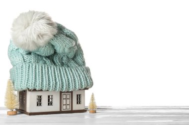 Masanın üzerinde beyaz arka planda şapka ve dekoratif köknar ağaçları olan ev modeli. Isıtma kavramı