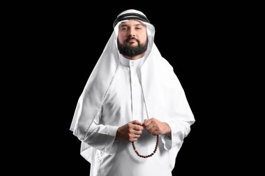 Siyah arkaplanda tespih taşıyan Müslüman bir adam.