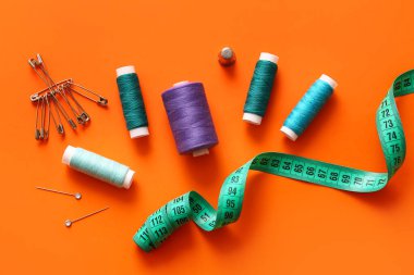 Turuncu zemin üzerinde iğne ve mezura bulunan iplik makaraları