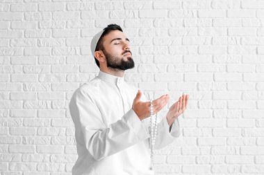 Beyaz tuğlalı arka planda dua eden genç Müslüman adam.