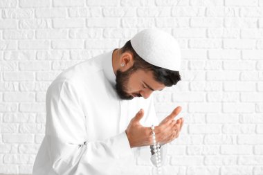 Beyaz tuğlalı arka planda dua eden genç Müslüman adam.
