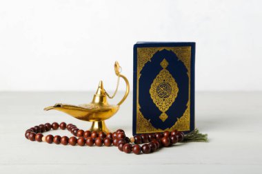Kuran, lamba ve beyaz ahşap masada tespih.