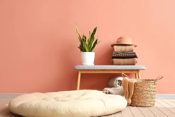 Stack of sweaters, felt hat on bench, basket and pouf near color wall in room