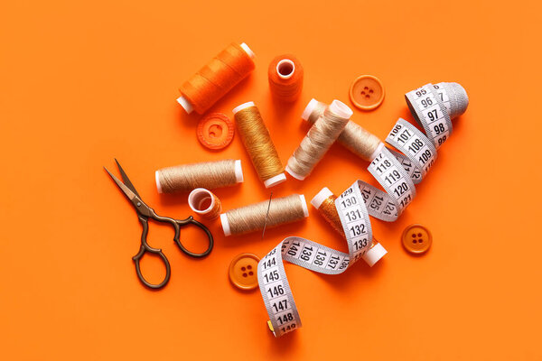 Катушки, измерительная лента, ножницы и кнопки на оранжевом фоне