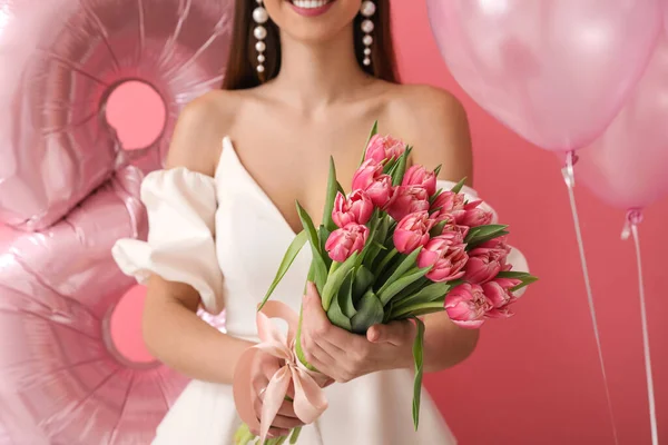 Stylish young woman with tulips and balloons on pink background. International Women\'s Day