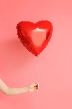 Pembe arka planda Sevgililer Günü kutlaması için kalp şeklinde güzel bir balonu olan bir kadın eli.