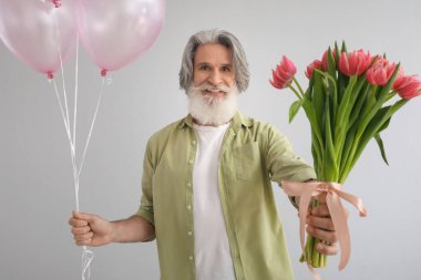 Kıdemli adam arka planda bir buket lale ve hava balonu tutuyor. Uluslararası Kadınlar Günü kutlamaları