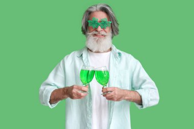 Yeşil arka planda bira bardakları olan gözlüklü son sınıf öğrencisi. Aziz Patrick Günü kutlaması