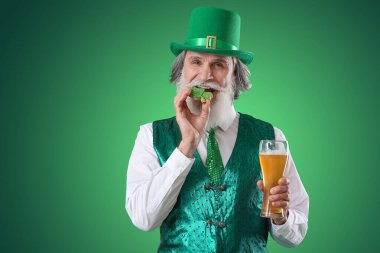 Yeşil arka planda bir bardak birayla kurabiye yiyen son sınıf öğrencisi. Aziz Patrick Günü kutlaması