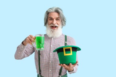 Mavi arka planda şapkası ve bir bardak birası olan son sınıf öğrencisi. Aziz Patrick Günü kutlaması