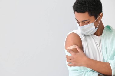 Hafif arka planda uygulamalı tıbbi yaması olan maskeli genç bir Afro-Amerikalı.
