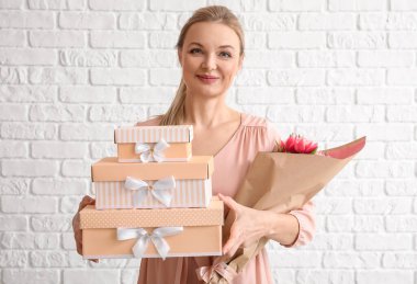 Beyaz tuğlalı arka planda bir buket lale ve hediye kutusu olan bir kadın. Uluslararası Kadınlar Günü kutlamaları