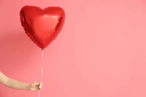 ピンクを背景にバレンタインデーのお祝いのための美しいハート型の風船を持つ女性の手 — ストック写真