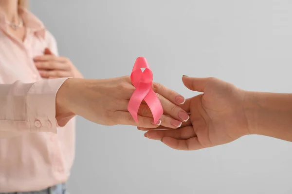 Woman with pink awareness ribbon shaking hands on light background, closeup. Breast cancer awareness concept