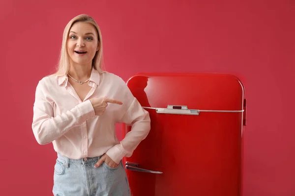 情绪激动的女人指着红色背景的时髦冰箱 — 图库照片