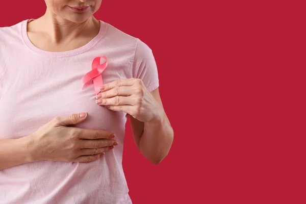 Woman with pink awareness ribbon on chest against red background, closeup. Breast cancer awareness concept