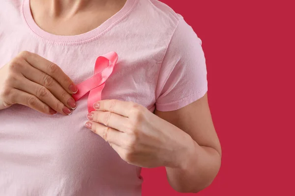 Woman adjusting pink awareness ribbon on chest against red background, closeup. Breast cancer awareness concept