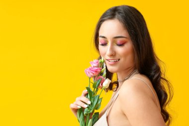 Yaratıcı makyajlı ve gözleri kapalı bir kadın sarı arka planda Eustoma çiçekleri tutuyor. Uluslararası Kadınlar Günü