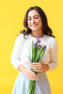 Sarı arka planda süsen çiçekleri tutan yaratıcı makyajlı mutlu kadın. Uluslararası Kadınlar Günü