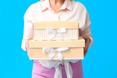Mavi arka planda hediye kutularını tutan olgun bir kadın, yakın plan. Uluslararası Kadınlar Günü kutlamaları