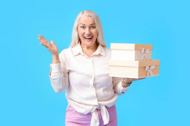 Duygusal olgun kadın mavi arka planda hediye kutuları tutuyor. Uluslararası Kadınlar Günü kutlamaları