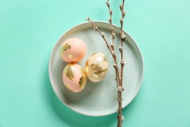 Plate with beautiful Easter eggs and pussy willow branches on color background
