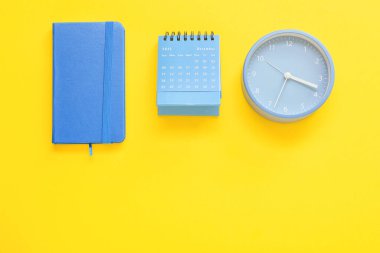 Sarı arkaplanda defter, takvim ve alarm saati