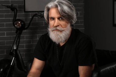 Yakışıklı, olgun sakallı bir adamın portresi. Evdeki koltukta oturuyor.