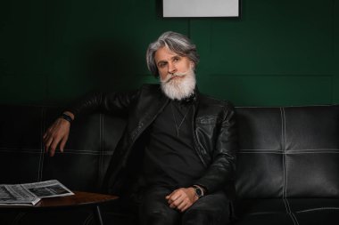 Evdeki kanepede oturan yakışıklı, olgun sakallı adamın portresi.