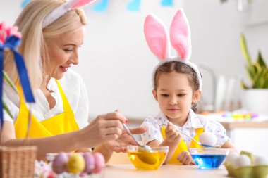 Küçük kız ve büyükannesi evde paskalya yumurtası boyuyor.