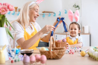 Küçük kız ve büyükannesi evde paskalya yumurtası boyuyor.