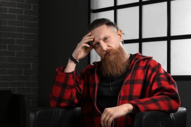 Evdeki koltukta oturan yakışıklı sakallı adamın portresi.