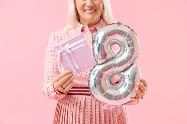Olgun bir kadın pembe arka planda hediye paketi ve balon tutuyor, yakın plan. Uluslararası Kadınlar Günü kutlamaları