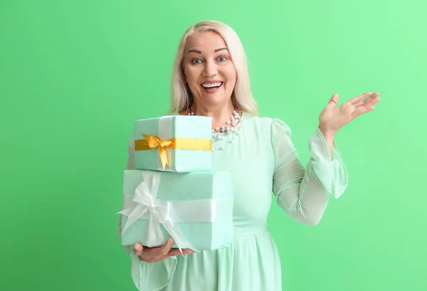 Uśmiechnięta Dojrzała Kobieta Trzymająca Stos Pudełek Prezentami Wskazująca Coś Zielonym — Zdjęcie stockowe