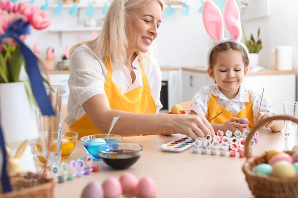 Küçük kız ve büyükannesi evde paskalya yumurtası boyuyor.