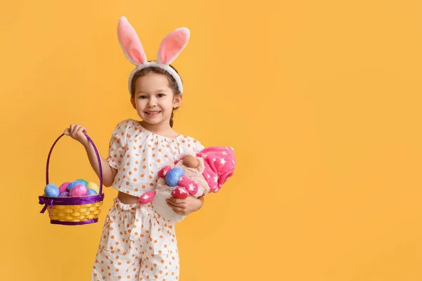 有趣的小女孩 有兔子耳朵 玩具和黄色背景的复活节篮子 — 图库照片