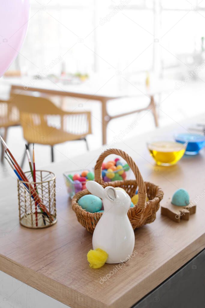 Basket with Easter eggs and figure of bunny with brushes on table in kitchen