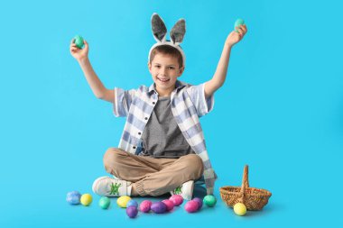 Mavi arka planda tavşan kulaklı ve paskalya yumurtaları olan komik bir çocuk.