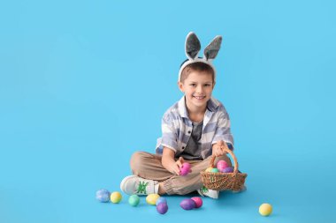 Mavi arka planda tavşan kulaklı ve paskalya yumurtaları olan komik bir çocuk.
