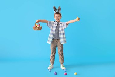 Tavşan kulaklı ve mavi arka planda Paskalya sepeti olan komik küçük çocuk.