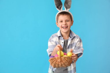 Tavşan kulaklı ve mavi arka planda Paskalya sepeti olan komik küçük çocuk.