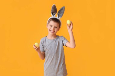 Tavşan kulaklı ve sarı arka planda Paskalya yumurtaları olan komik küçük çocuk.