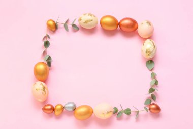 Paskalya yumurtaları ve pembe arka planda okaliptüs dallarından yapılmış çerçeve