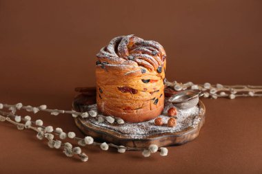Wooden board with delicious Easter cake and pussy willow branches on brown background